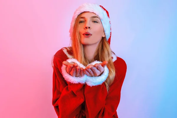 Affascinante giovane donna in Santa hat stand e invia un bacio su sfondo luce al neon — Foto Stock