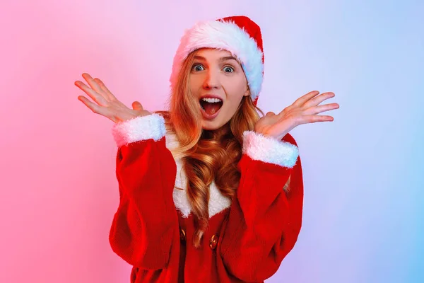 Uma imagem de uma jovem excitada chocada, usando um chapéu de Papai Noel, em pé contra um fundo com luz de néon . — Fotografia de Stock