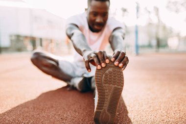 Afro-Amerikan atletizmi germe egzersizleri yapıyor, stadyumda sabah antrenmanına hazırlanıyor.
