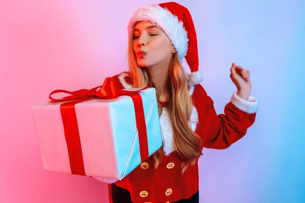 Щаслива дівчина з Санта - Капелюха тримає на задньому плані велику коробку з подарунками. — стокове фото