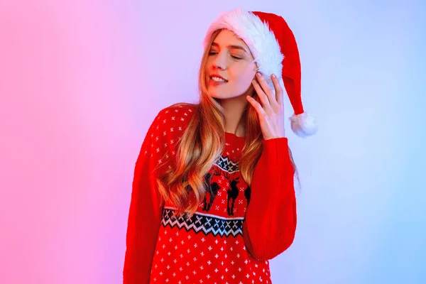 Atraktivní mladá žena v klobouku Santa pózuje na pozadí neonových světel — Stock fotografie