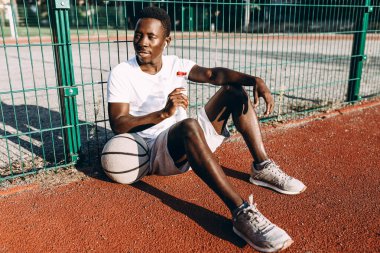 Afrikalı Amerikalı bir şişe suyla antrenman yaptıktan sonra dinleniyor ve kulaklıkla müzik dinliyor.