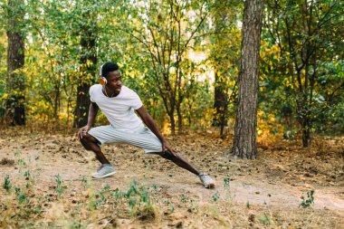 Atletik Afro-Amerikalı adam gerinme egzersizleri yapıyor, parkta sabah antrenmanına hazırlanıyor.