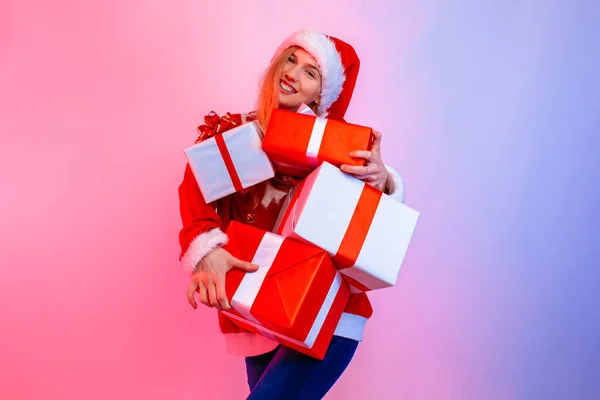Šťastná vzrušená mladá žena nosí Santa klobouk drží mnoho krabic stojící na pozadí — Stock fotografie