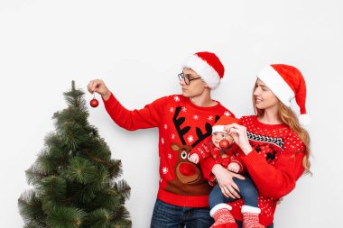 Noel şapkalı mutlu aile, anne baba ve küçük çocuk Noel 'i kutluyor ve Noel ağacını süslüyor..