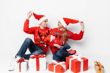 Noel Baba şapkalı mutlu bir aile oturmuş Noel 'i hediyelerle kutluyor.