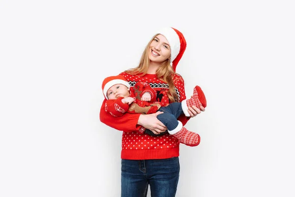 Jonge moeder in santa hoed met kleine baby in santa kostuum staande op witte achtergrond — Stockfoto