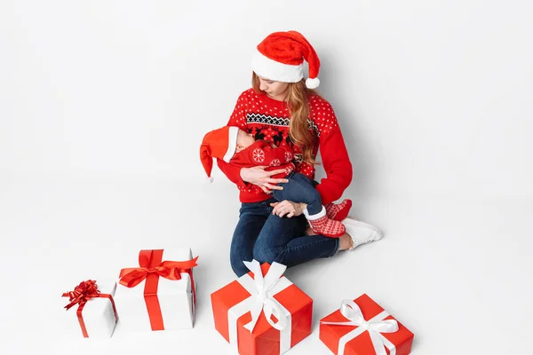 Junge Mutter mit Weihnachtsmütze und kleinem Baby im Weihnachtsmannkostüm auf weißem Hintergrund — Stockfoto