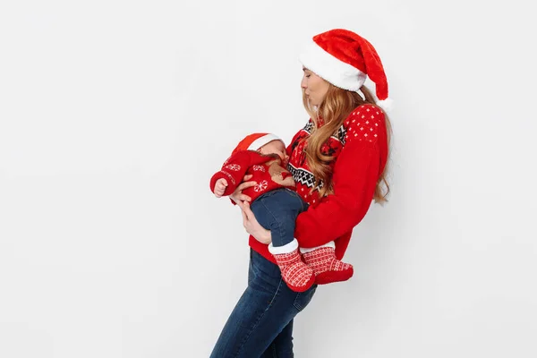 Jonge moeder in santa hoed met kleine baby in santa kostuum staande op witte achtergrond — Stockfoto
