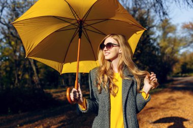 Sarı şemsiyeli kız, sonbahar zamanı, sarı yapraklı parkta.