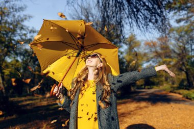Sarı şemsiyeli mutlu kız, Parktaki sonbahar sıcağının tadını çıkarıyor.