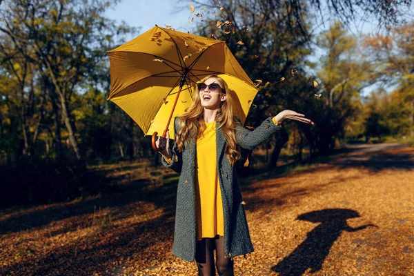 Glückliches Mädchen mit gelbem Regenschirm, das die herbstliche Wärme im Park genießt — Stockfoto