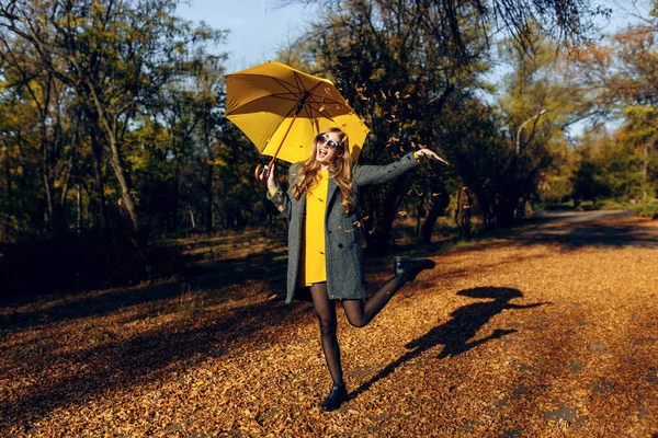 Glückliches Mädchen mit gelbem Regenschirm, das die herbstliche Wärme im Park genießt — Stockfoto