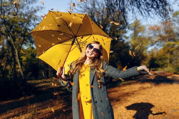 Ευτυχισμένο κορίτσι, με μια κίτρινη ομπρέλα, απολαμβάνοντας τη ζεστασιά του φθινοπώρου στο πάρκο — Φωτογραφία Αρχείου