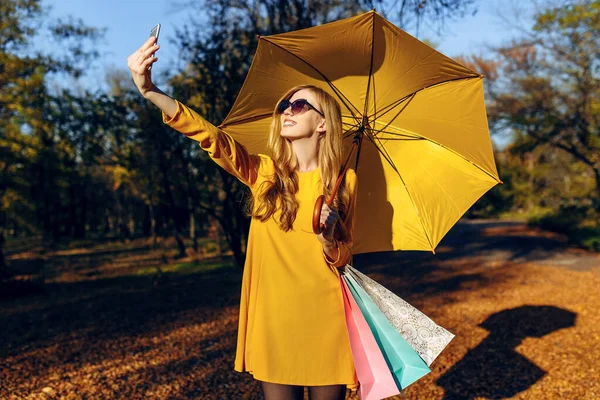 Stylisches Mädchen macht nach dem Einkaufen auf der Straße ein Selfie mit ihrem Smartphone und hält Taschen in der Hand — Stockfoto