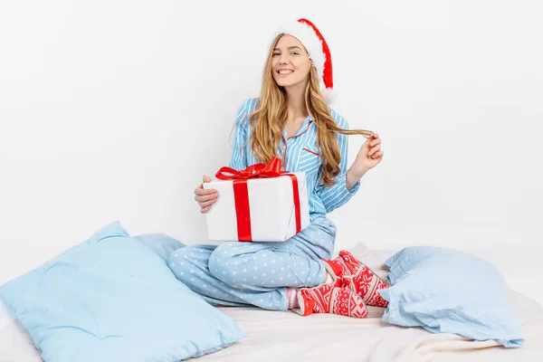 Weihnachtsmorgen. glückliches schönes junges Mädchen, in weihnachtlichem Pyjama und Weihnachtsmütze, erhielt an Weihnachten ein Geschenk — Stockfoto