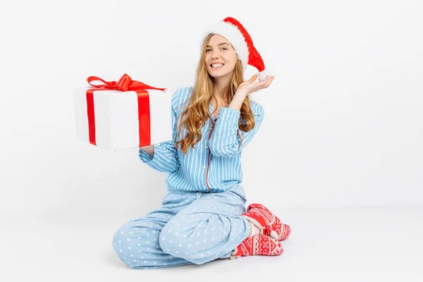 Christmas morning. Happy beautiful young girl, in Christmas pajamas and Santa hat, opens Christmas gift — Stock Photo, Image