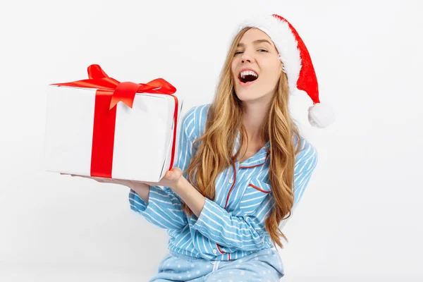 Boże Narodzenie rano. Szczęśliwa piękna młoda dziewczyna, w piżamie i kapeluszu Mikołaja, jest szczęśliwy, aby otrzymać prezent — Zdjęcie stockowe