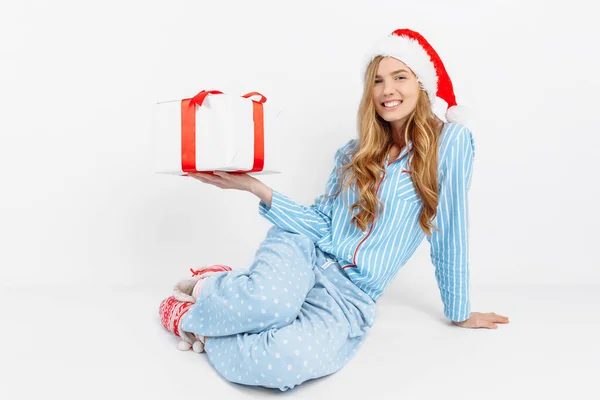 Manhã de Natal. Menina bonita feliz, em pijama de Natal e chapéu de Papai Noel, está feliz em receber um presente — Fotografia de Stock