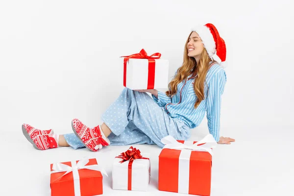 Χριστουγεννιάτικο πρωινό. Ευτυχισμένο όμορφο νεαρό κορίτσι, με τις χριστουγεννιάτικες πιτζάμες και το καπέλο του Αϊ Βασίλη, έλαβε πολλά δώρα Χριστουγέννων — Φωτογραφία Αρχείου