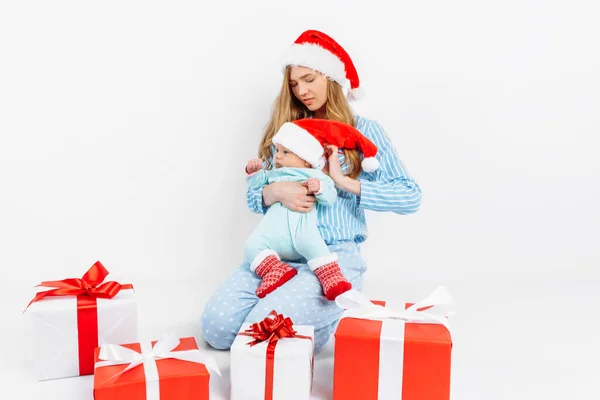 Een jonge moeder, op kerstdag geeft een geschenk aan een pasgeboren kind, een meisje houdt een baby in haar armen met een kerstcadeau — Stockfoto