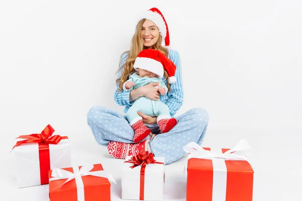 Een jonge moeder, op kerstdag geeft een geschenk aan een pasgeboren kind, een meisje houdt een baby in haar armen met een kerstcadeau — Stockfoto