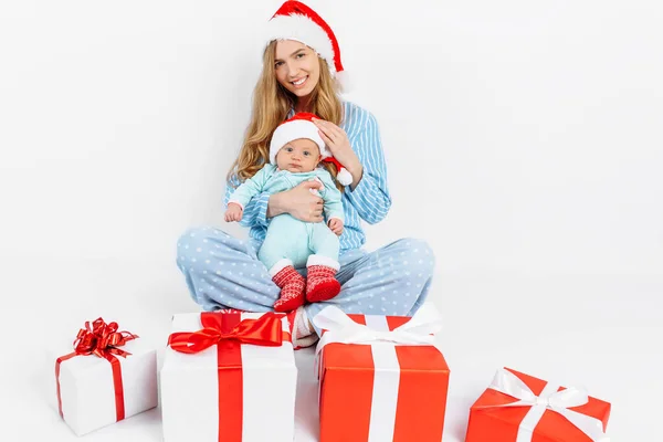 Een jonge moeder, op kerstdag geeft een geschenk aan een pasgeboren kind, een meisje houdt een baby in haar armen met een kerstcadeau — Stockfoto