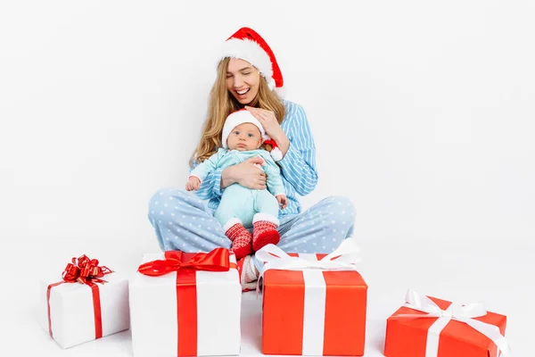 Een jonge moeder, op kerstdag geeft een geschenk aan een pasgeboren kind, een meisje houdt een baby in haar armen met een kerstcadeau — Stockfoto