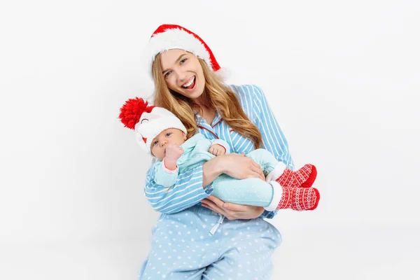 Een jonge moeder, op kerstdag geeft een geschenk aan een pasgeboren kind, een meisje houdt een baby in haar armen in een kerstmuts — Stockfoto