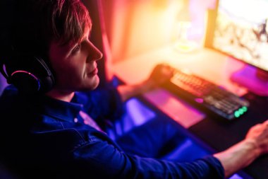 Profesyonel oyuncu kulaklıkla bilgisayar oyunları oynuyor, neon ışıklı bir odada..