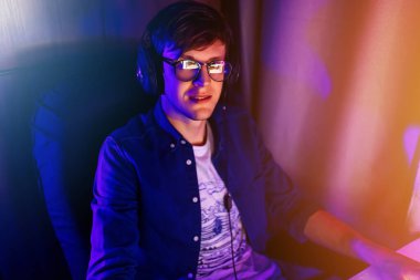 Profesyonel bir oyuncu, kişisel bilgisayarında neon ışıkları olan bir odada oturan ilk kişi ile çevrimiçi video oyunları oynar. Çevrimiçi siber spor şampiyonası.