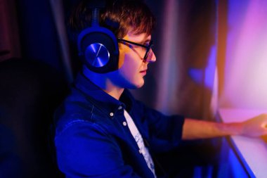 Profesyonel bir oyuncu, kişisel bilgisayarında neon ışıkları olan bir odada oturan ilk kişi ile çevrimiçi video oyunları oynar. Çevrimiçi siber spor şampiyonası.