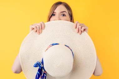 Mutlu genç bir kadın elinde bir şapka tutuyor ve izole edilmiş sarı bir arka planda duruyor.