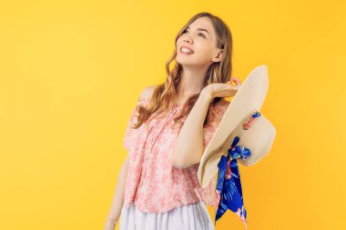 Mutlu genç bir kadın elinde bir şapka tutuyor ve izole edilmiş sarı bir arka planda duruyor.