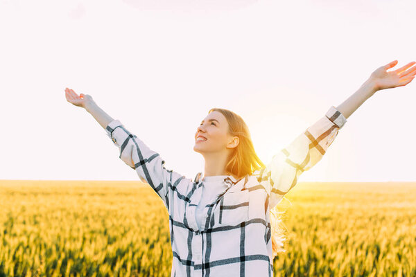 woman with outstretched arms in a wheat field against the background of the sunset