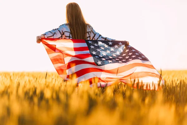 young happy girl runs and jumps with open arms across a wheat field. Holding the US flag