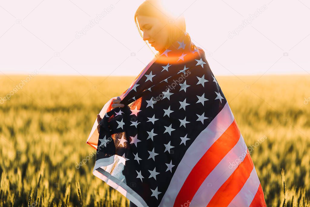 young happy woman, in a wheat field with an American flag on the background of the sunset