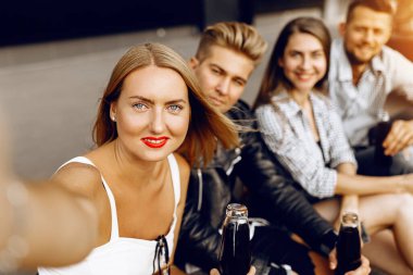 Bir grup neşeli arkadaş, oğlanlar ve kızlar parkta birlikte yürüyüp akıllı bir telefondan selfie çekiyorlar, eğleniyorlar ve içki içiyorlar.