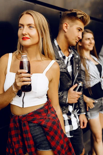 一群时髦的朋友 姑娘和小伙子在城里靠着一面黑墙散步 摆出姿势喝酒 — 图库照片