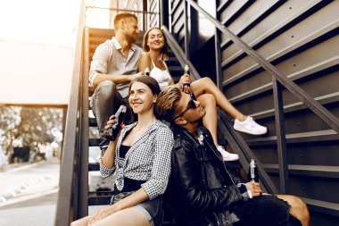 Genç okul arkadaşları merdivenlerde otururken cam şişelerde içki içiyorlar.