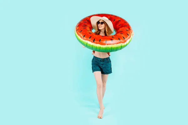 快乐的女孩 戴着太阳镜 泳衣和夏帽 站在一个充气的泳圈里 与蓝色背景隔离 — 图库照片