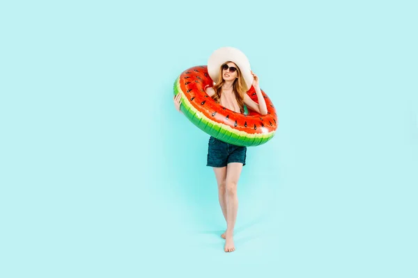 快乐的女孩 戴着太阳镜 泳衣和夏帽 站在一个充气的泳圈里 与蓝色背景隔离 — 图库照片