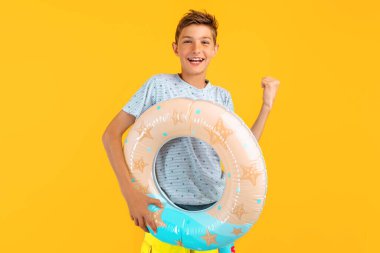 Mutlu genç adam şişme bir deniz çemberiyle ayakta duruyor ve sarı arka planda izole edilmiş kazanan bir jest gösteriyor. Yaz tatili kavramı