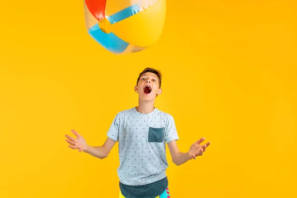 Happy excited teen guy playing beach ball isolated on yellow background. The concept of summer vacation