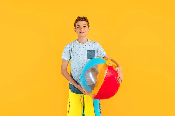Happy excited teen guy playing beach ball isolated on yellow background. The concept of summer vacation