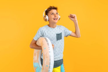Gülümseyen ergen, şişme yüzme çemberiyle, kulaklıkla müzik dinlerken, izole edilmiş sarı bir arka planda dururken kazanan bir jest yapıyor.
