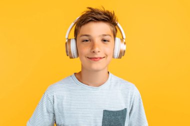 Gülümseyen genç kulaklıkla müzik dinliyor, izole edilmiş sarı bir arka planda duruyor.