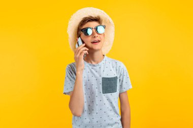 Sarı arka planda cep telefonuyla konuşan, yaz şapkalı şık, güler yüzlü genç adam.