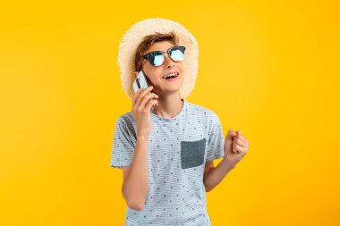Sarı arka planda cep telefonuyla konuşan, yaz şapkalı şık, güler yüzlü genç adam.