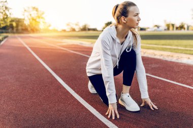 Spor giyimli atletik kız, yarışın başlangıç çizgisinde. Bir bayan koşucu, şafağın arka planına karşı başlangıç çizgisinden koşmaya başladı..